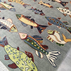 May include: A rectangular rug with a light grey background displaying a repeating pattern of colourful fish. The fish vary in size and colour, including shades of green, yellow, blue, and brown. The rug has a fringe along one edge.