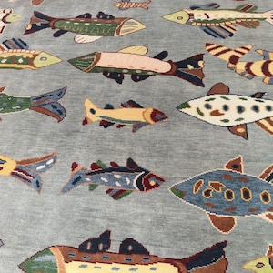 May include: A light blue rug featuring a repeating pattern of colourful fish. The fish vary in size and design, with shades of yellow, green, brown, and blue. The rug's background is a solid, muted blue.