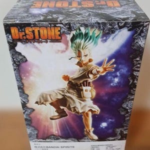 May include: A box featuring a vibrant illustration of a character from the anime series Dr. Stone. The character has green hair and is wearing a light-colored outfit. The box has the Dr. Stone logo and Japanese text.