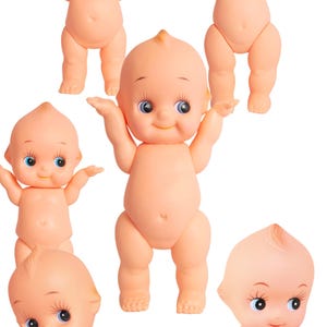 May include: A collection of six small, peach-colored baby dolls with large blue eyes and small tufts of yellow hair. The dolls are in various poses, including standing with arms raised and crawling.
