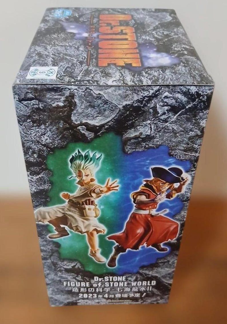 May include: A box featuring the Dr. Stone anime series. The box art shows two characters in action poses against a green and blue background. The text "Dr. Stone FIGURE of STONE WORLD" is visible, along with Japanese text and the date "2023年4月登場予定!"