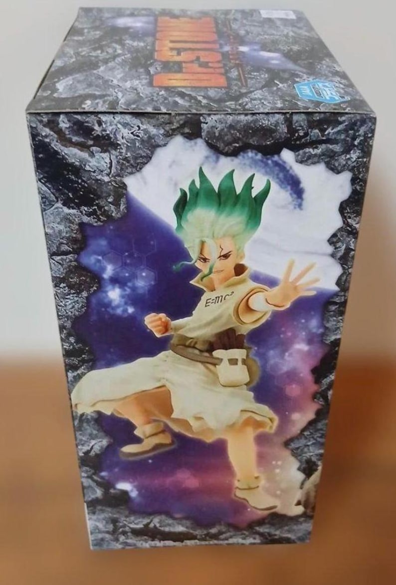 May include: A box featuring a colorful illustration of a character with green hair and a white outfit. The character is in a dynamic pose, with one arm outstretched. The box has a stone-like design on the top and sides.