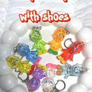 May include: A collection of colorful Kewpie doll keychains in various colors, including green, orange, blue, and purple. Each doll has a unique design and is attached to a silver keychain. The text "Unique Kewpie with shoes" is displayed at the top.