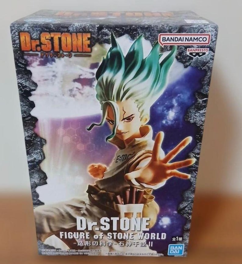 May include: A boxed Dr. Stone figure. The box features a character with green and white hair, a tan jacket, and the text "Dr. STONE" and "FIGURE of STONE WORLD". The background has a purple and blue galaxy design.