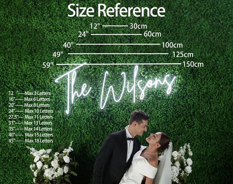 Puede incluir: Un letrero de ne&oacute;n con el texto "The Wilsons" se muestra sobre un fondo verde, con referencias de tama&ntilde;o en pulgadas y cent&iacute;metros. Una pareja se abraza frente al letrero, con flores blancas en primer plano.
