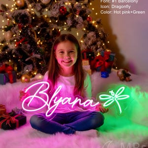 Puede incluir: Un letrero de ne&oacute;n personalizado con el nombre Blyana en letras cursivas de color rosa intenso y un icono de lib&eacute;lula verde. El letrero mide 90 cm de ancho. El texto en la imagen especifica: Size: 35"/90cm, Font: #1 Barcelony, Icon: Dragonfly, Color: Hot pink+Green.