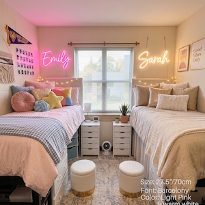 Puede incluir: Dos letreros de ne&oacute;n personalizados con los nombres Emily en rosa y Sarah en blanco c&aacute;lido. Los letreros miden 70 cm de ancho y utilizan la fuente Barcelona. Est&aacute;n montados en una pared sobre dos camas individuales en un dormitorio compartido.