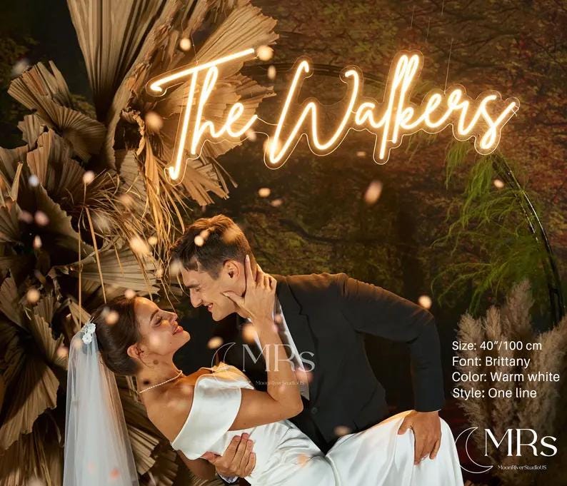 Puede incluir: Un letrero de ne&oacute;n blanco c&aacute;lido muestra "The Walkers" en una fuente cursiva. El letrero cuelga sobre una pareja. El letrero mide 100 cm de ancho, con una fuente Brittany y un estilo de una l&iacute;nea. El fondo presenta plantas secas.