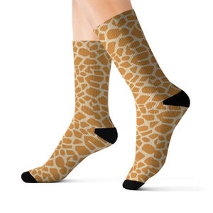 May include: A pair of socks with a giraffe print. The socks are tan and white with a black heel and toe.