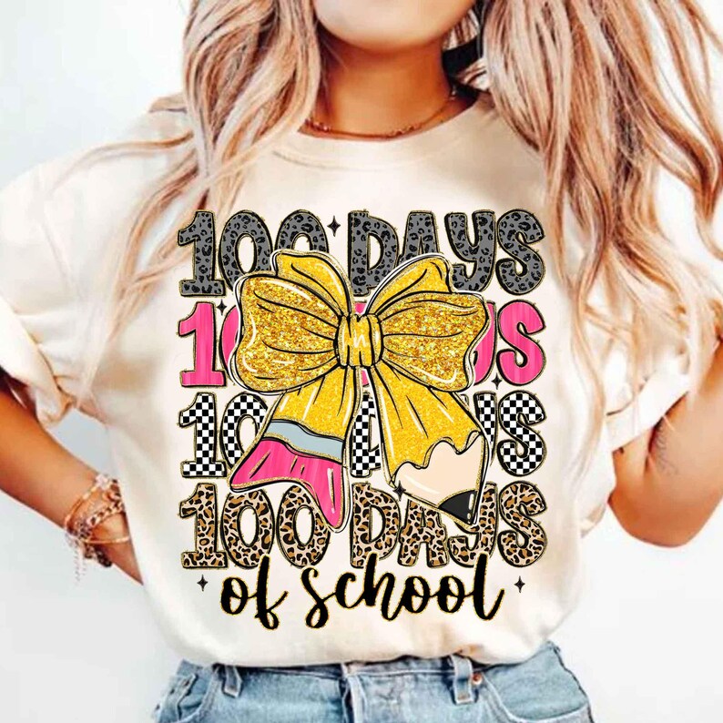 Puede incluir: Camiseta color crema con un gr&aacute;fico colorido que celebra los 100 d&iacute;as de escuela. El dise&ntilde;o presenta un gran lazo amarillo con purpurina, un l&aacute;piz y el texto "100 Days of School". El texto est&aacute; en una mezcla de fuentes y patrones.