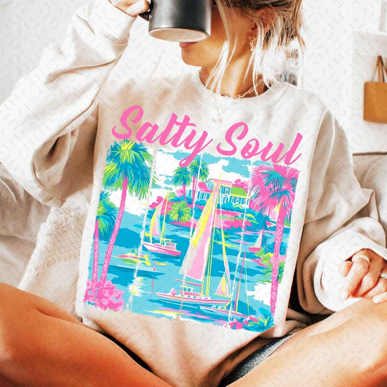 May include: A white sweatshirt with a pink graphic of palm trees, sailboats, and the text "Salty Soul".