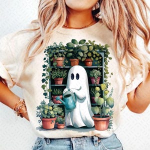 Könnte beinhalten: Ein weißer Geist mit einer blauen Gießkanne gießt Pflanzen auf einem Regal. Der Geist lächelt und hat zwei schwarze Augen. Das Regal ist gefüllt mit grünen Pflanzen in braunen Töpfen.