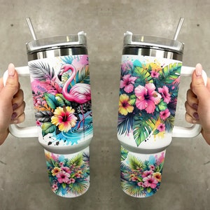 Pu&ograve; includere: Due tazze da viaggio in acciaio inossidabile bianco con manici e coperchi. Una tazza presenta un fenicottero rosa in piedi in una pozza d'acqua circondata da fiori e foglie tropicali. L'altra tazza presenta un gruppo di fiori di ibisco rosa e gialli con foglie verdi. Entrambe le tazze hanno uno sfondo bianco con schizzi di colore simili ad acquerello.