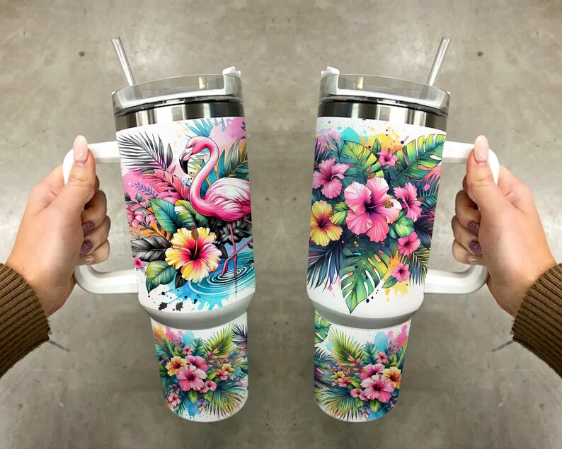 Pu&ograve; includere: Due tazze da viaggio in acciaio inossidabile bianco con manici e coperchi. Una tazza presenta un fenicottero rosa in piedi in una pozza d'acqua circondata da fiori e foglie tropicali. L'altra tazza presenta un gruppo di fiori di ibisco rosa e gialli con foglie verdi. Entrambe le tazze hanno uno sfondo bianco con schizzi di colore simili ad acquerello.