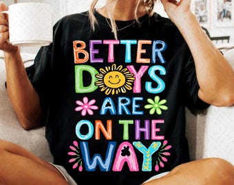 May include: Black t-shirt with the text "Better Days Are On The Way" in colorful letters. A smiling sun and flowers are included in the design.