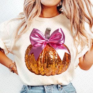 May include: A gold glitter pumpkin with a large pink bow. The pumpkin is a festive autumn decoration.