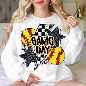 Może przedstawiać: Biała bluza z nadrukiem graficznym przedstawiającym wz&oacute;r w kratkę, błyskawicę, dwa wzory piłek miękkich i tekst "GAME DAY".