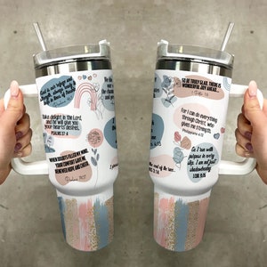 K&ouml;nnte beinhalten: Ein wei&szlig;er Becher mit Henkel und Strohhalm. Der Becher ist mit verschiedenen inspirierenden Zitaten und Designs verziert, darunter Blumen, Herzen und Pinselstriche in Rosa, Blau und Gold. Die Zitate beinhalten "Gott ist unsere Zuflucht und St&auml;rke, immer bereit, in Zeiten der Not zu helfen." und "Freut euch also wahrhaft. Es gibt eine wunderbare Freude vor euch."