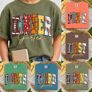 May include: A collection of short-sleeved t-shirts in various colours including olive, orange, brown, green, and blue. Each shirt features a graphic print with sports-themed patterns inside the letters spelling out grade levels like Kindergarten.