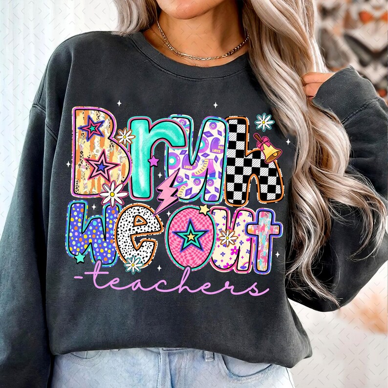 Op de afbeelding: Een donkergrijs sweatshirt met een kleurrijke grafische print die "Bring We Out - teachers" zegt. De grafiek is gemaakt van verschillende patronen en kleuren, waaronder sterren, bliksem en bloemen.
