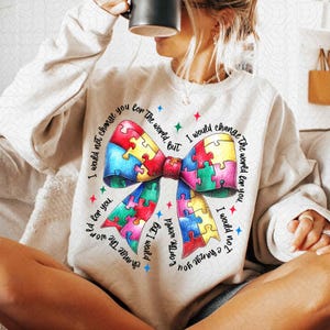 May include: A light beige sweatshirt with a colorful puzzle piece bow and the text "I would not change you for the world, but I would change the world for you."