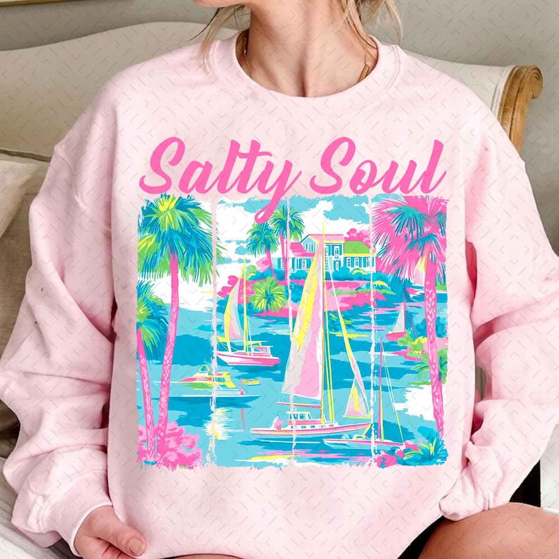 May include: Pink sweatshirt with a graphic of palm trees, sailboats, and a house. The text "Salty Soul" is printed in pink on the sweatshirt.