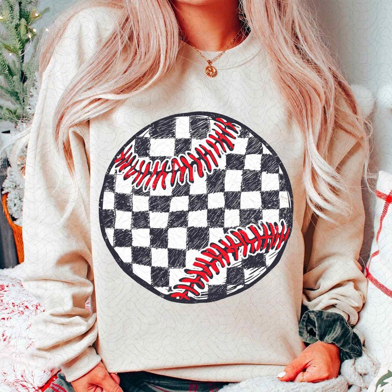 May include: A beige sweatshirt featuring a large, circular graphic of a baseball. The baseball design has a black and white checkered pattern with red stitching details. The sweatshirt has long sleeves.
