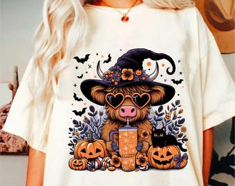 May include: A white t-shirt with a cartoon illustration of a highland cow wearing a witch hat, sunglasses, and holding a pumpkin spice latte. The cow is surrounded by pumpkins, candy, and bats.