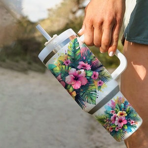 Pu&ograve; includere: Un bicchiere in acciaio inossidabile bianco con un design floreale tropicale che presenta fiori di ibisco rosa, foglie verdi e un tocco di vernice gialla. Il bicchiere ha un coperchio e un manico.
