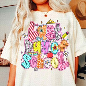 Pode incluir: Uma camiseta branca com um gr&aacute;fico colorido que diz "&Uacute;ltimo dia de aula" com v&aacute;rios materiais escolares e outros desenhos.