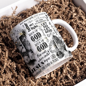 Peut inclure: Une tasse en céramique blanche avec un motif noir et blanc représentant des mains en prière, une croix et du texte qui dit "Love never fails gives wisdom Alpha and Omega The Lord our righteous light Let go Let God Man of God Man of God Fear ends where faith begins Jesus Lord faithful The Lord is peace".