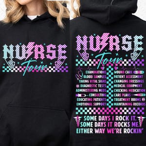 May include: Black hoodie with a pink, blue, and white checkered design and the text "NURSE TOUR" in a bold, stylized font. The back of the hoodie features a list of tasks a nurse performs, including "examinations", "wound care", "blood samples", "patient assessment", "taking vital signs", "changing dressings", "diagnostic tests", "medical equipment", "administering meds", "checking medication", "consulting", "care plans", "educating patients", "treatment rooms", "emotional support", and "maintaining records". The bottom of the hoodie features the text "SOME DAYS I ROCK IT. SOME DAYS IT ROCKS ME. EITHER WAY WE'RE ROCKIN'" in a pink, blue, and white checkered design.