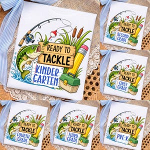 May include: A white t-shirt featuring a graphic of a fishing rod, a green fish, a wooden sign reading READY TO TACKLE, a yellow pencil, and a green tackle box. Below the sign, a blue notebook paper graphic displays various grade levels.