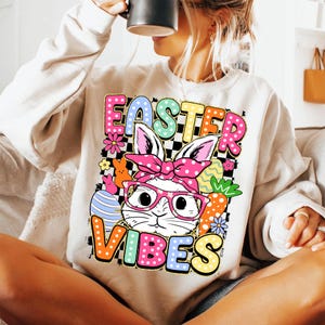 May include: A white sweatshirt with a colorful graphic design featuring a bunny wearing glasses and a pink bandana. The graphic also includes the text "Easter Vibes" in colorful letters.