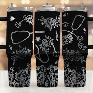 May include: Three black stainless steel tumblers with a white floral design and medical symbols, including a stethoscope, pills, a syringe, a thermometer, and a face mask. The tumblers have a handle and a lid.