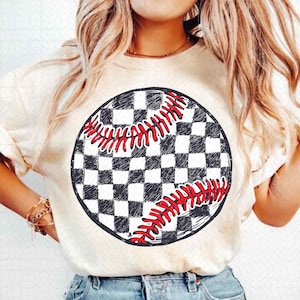 May include: Cream-colored t-shirt featuring a baseball design. The baseball graphic is a black and white checkered circle with red stitching. The shirt has short sleeves and a crew neck.