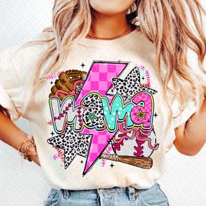 Może przedstawiać: Biały T-shirt z nadrukiem graficznym przedstawiającym słowo "mama" w kolorowych literach z różowym błyskawicą, piłką baseballową i rękawicą baseballową. Projekt zawiera również wzór w czarno-białe cętki.