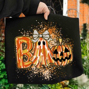 May include: Black Halloween graphic with the word "BOO" in orange and gold, a ghost with a bow, and a jack-o'-lantern. The design includes orange and gold splatter effects, ideal for Halloween celebrations.