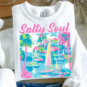 May include: White sweatshirt with a pink graphic that says "Salty Soul" and features a beach scene with palm trees, sailboats, and a house.