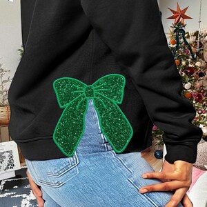 May include: Black sweatshirt with a green glitter bow on the back. The bow is a large, sparkly design.