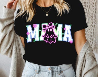 Può includere: Maglietta nera con una grafica bianca "MAMA" che presenta un fantasma con un fiocco rosa. Il fantasma è delineato in rosa, verde e blu.