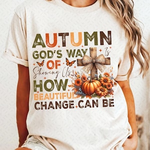 May include: A white t-shirt with a fall-themed design featuring a cross, pumpkins, butterflies, and the text "Autumn God's Way of Showing Us How Beautiful Change Can Be."
