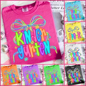 May include: A collection of colorful t-shirts with grade-level designs. The pink shirt displays "Kindergarten" in vibrant colors with a bow graphic. Other shirts feature "Pre-School", "Pre-K", "First Grade", "Fifth Grade", "Fourth Grade", "Third Grade", and "Second Grade".