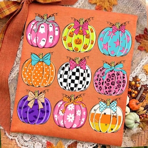 May include: An orange fabric sheet featuring a grid of nine decorative pumpkins. Each pumpkin displays a unique pattern, including ghosts, jack-o'-lanterns, stars, polka dots, checkers, leopard print, bats, flowers, and stripes, all topped with bows.