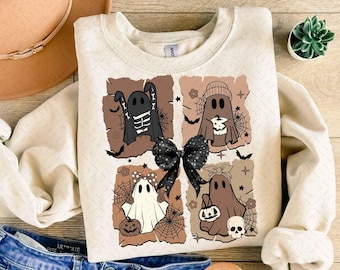 May include: A cream-colored sweatshirt with a graphic of four ghosts in different poses. The ghosts are wearing costumes and holding Halloween treats. The background is a brown and tan color with a black bow.