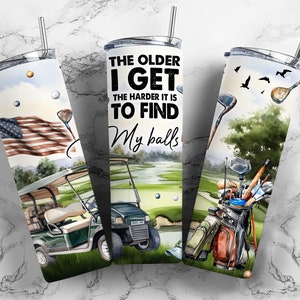 May include: A set of three stainless steel tumblers with a golf theme. The tumblers feature a watercolor design of a golf course, golf clubs, and a golf cart. The text on the tumbler reads "The older I get the harder it is to find my balls".
