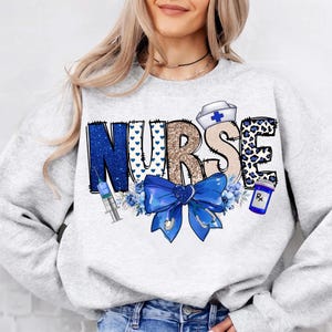 May include: A gray sweatshirt with the word "NURSE" in blue, gold, and white glitter letters. The letters are decorated with blue hearts, a blue bow, a blue and white syringe, a blue and white pill bottle, and a white nurse's hat with a blue cross.