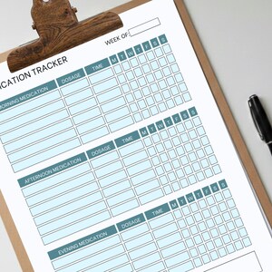 Könnte beinhalten: Ein Medikamententracker auf einem Klemmbrett mit einer Holzklammer. Der Tracker hat Abschnitte für Morgen-, Nachmittags- und Abendmedikation mit Feldern für Dosierung und Uhrzeit. Ein schwarzer Stift liegt daneben.