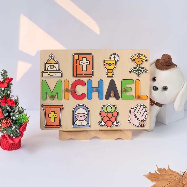 May include: A wooden puzzle board with the name "MICHAEL" spelled out in colorful letters. The board features various religious icons, including a church, a cross, a chalice, a bible, a nun, a flower, and a hand with a cross.