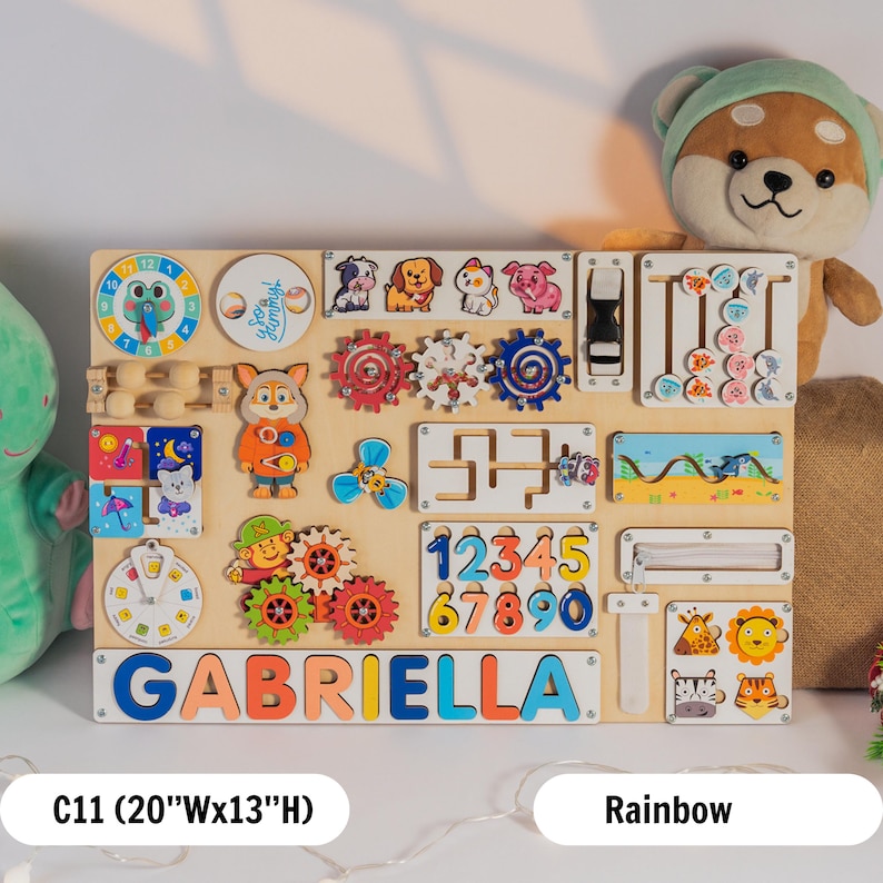 May include: A colourful wooden activity board for toddlers with various activities, including a clock, gears, a maze, numbers, a zipper, and a sliding door. The board is personalised with the name "GABRIELLA" in colourful letters. The board is 20 inches wide and 13 inches high.